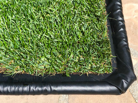 Corner of a black PVC flex-tray holding a real grass dog potty pad on a stone patio.